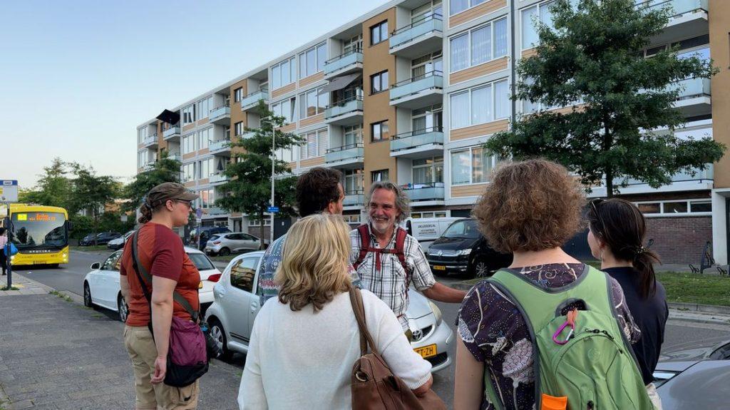 Deelnemers van de buurtsafari in Kanaleneiland staan bij elkaar en luisteren naar hovenier Rob van der Steen