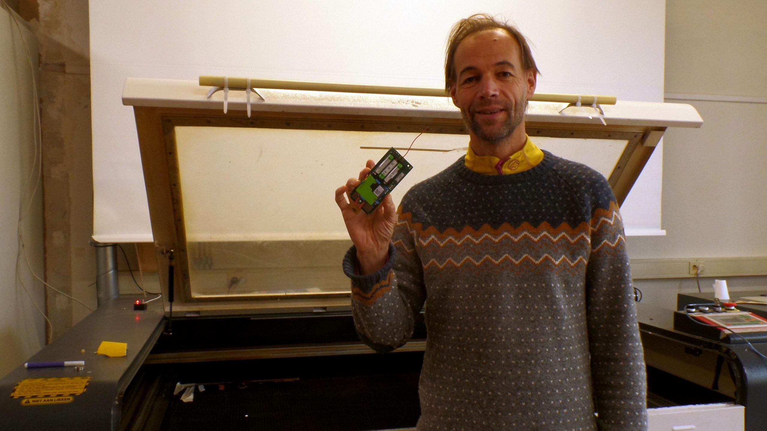 Egon Kastelijn die vrolijk lacht en een meetkastje ophangt